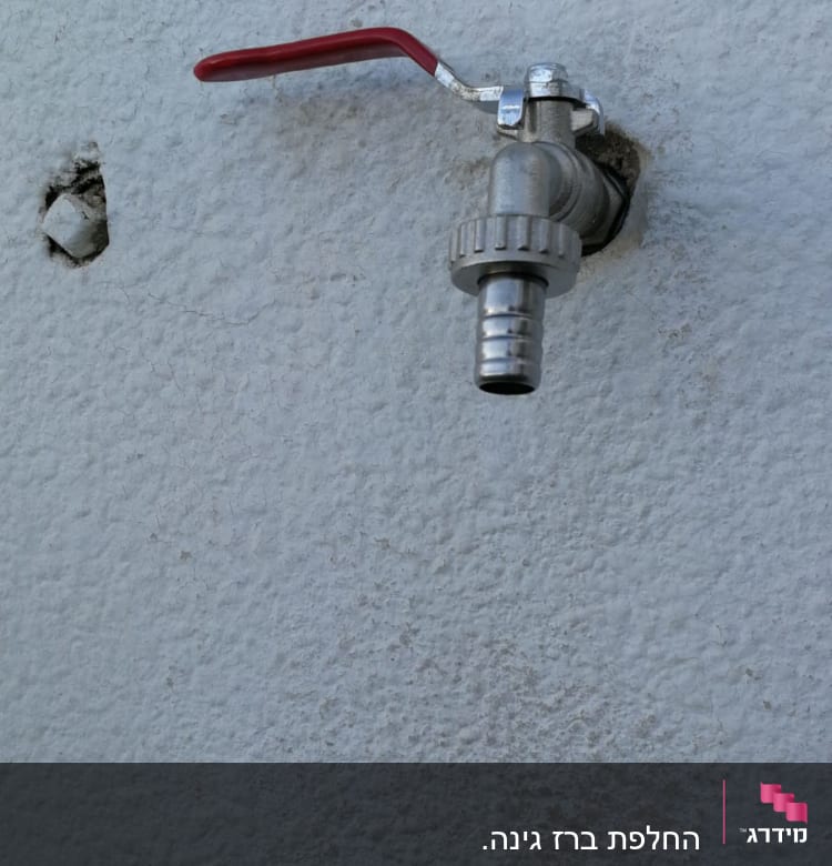 ברז מתכת עם ידית אדומה על קיר